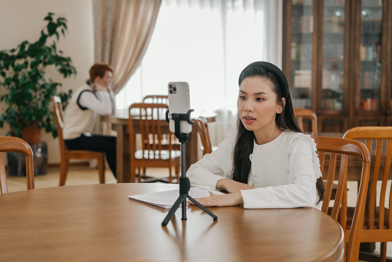 Young woman creating vlog content using a smartphone in a cozy indoor setting with wooden furniture.
